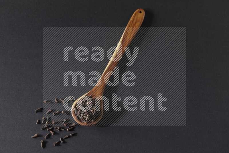 A wooden ladle full of whole cloves on a black flooring