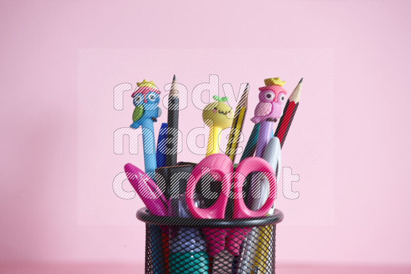 Pens, pencils and other different school supplies in a metal pen holder on rose background