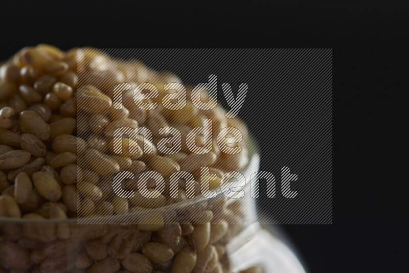 Hulled wheat in a glass jar on black background