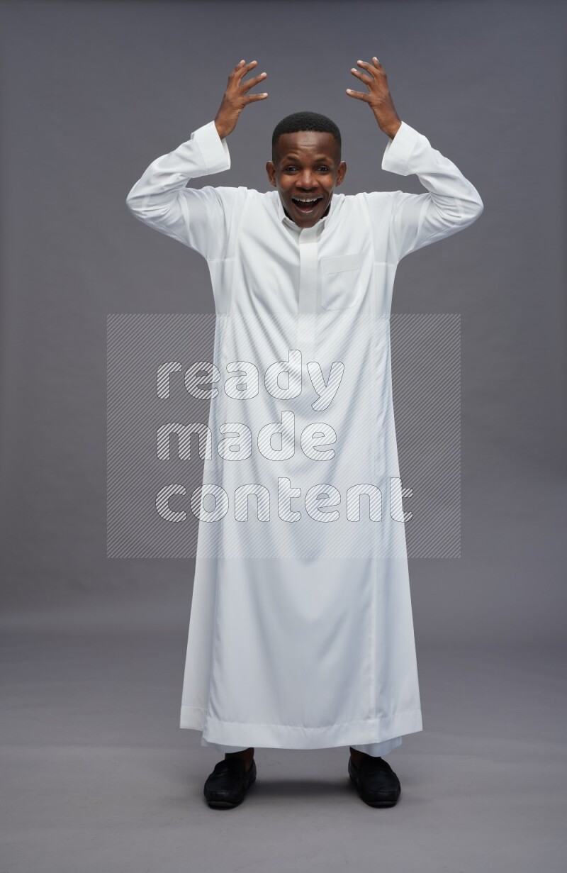 Saudi man wearing thob standing hands behind head on gray background