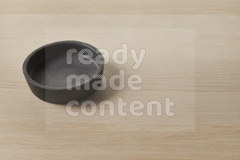 A black pottery bowl on light wooden background