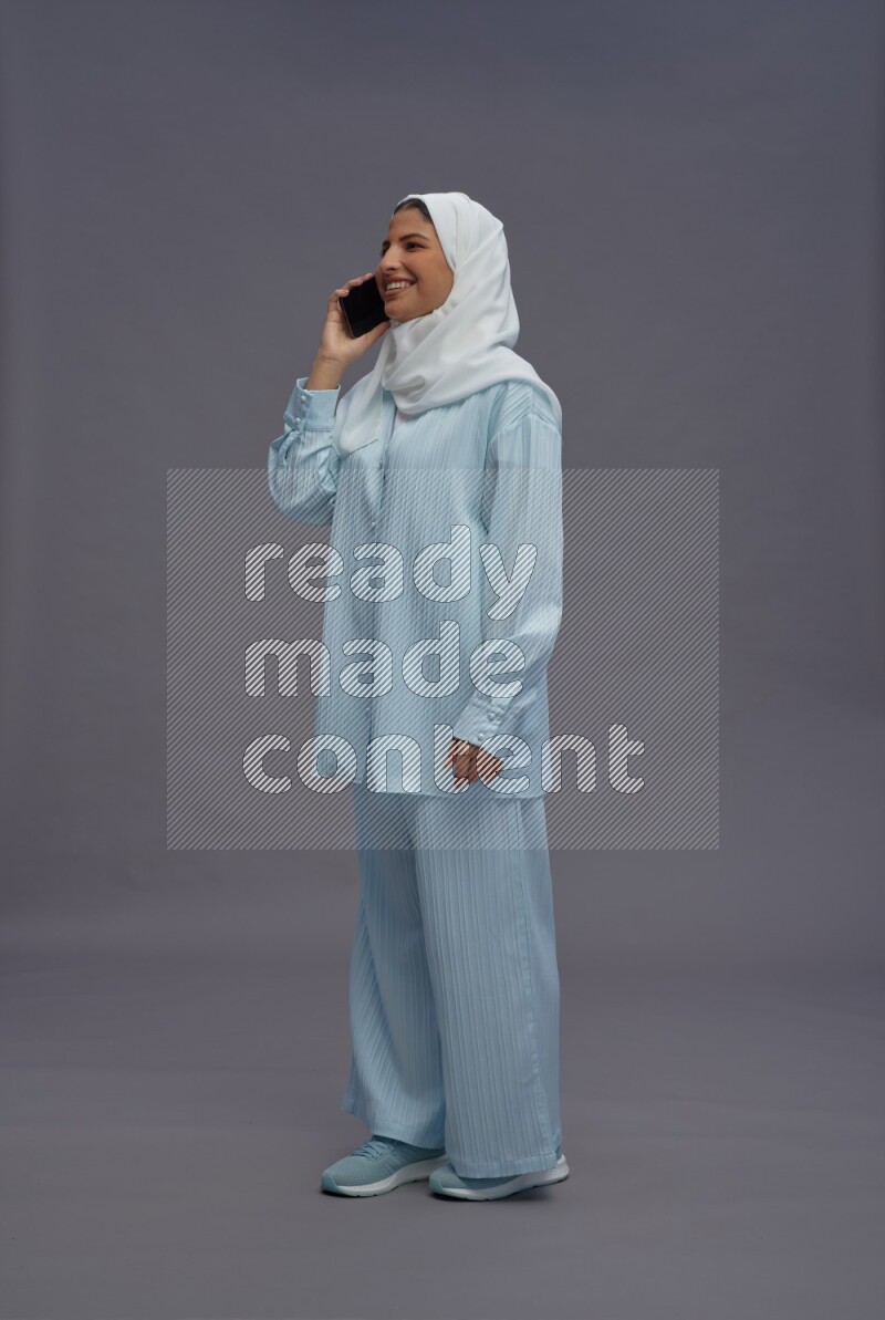 Saudi woman wearing hijab clothes standing talking on phone on gray background