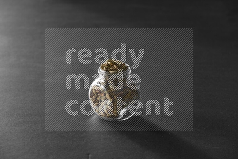 A glass spice jar full of cardamom on black flooring