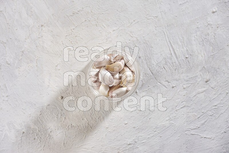 A glass jar full of garlic cloves on a textured white flooring