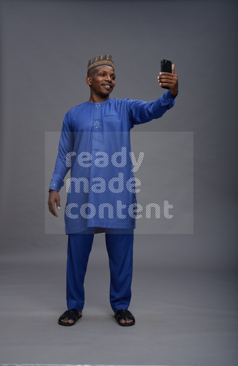Man wearing Nigerian outfit standing taking selfie on gray background