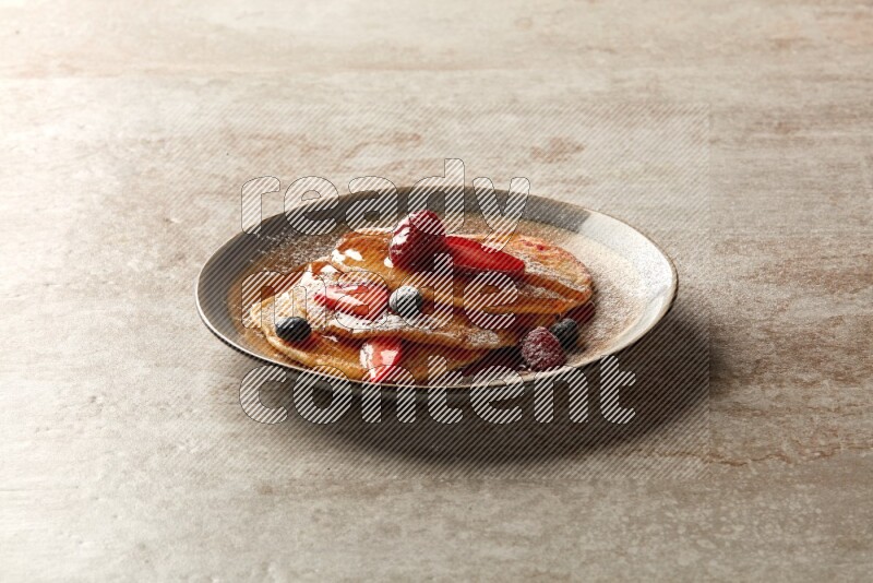 Three stacked mixed berries pancakes in a bicolor plate on beige background