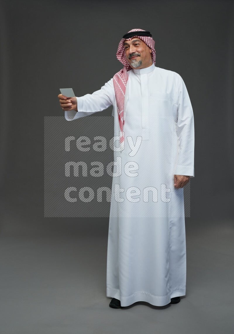 Saudi man with shomag Standing holding ATM card on gray background