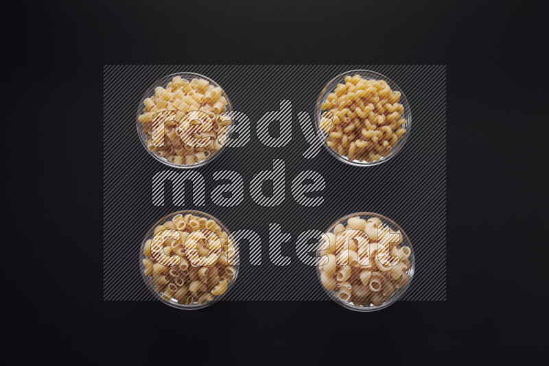 Different pasta types in glass bowls on black background
