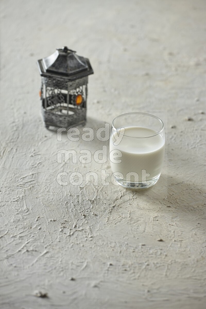 A silver lantern with different drinks, dates, nuts, prayer beads and quran on textured white background