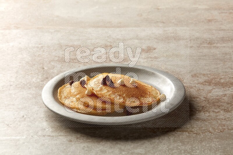 Three stacked chocolate chips pancakes in a grey plate on beige background