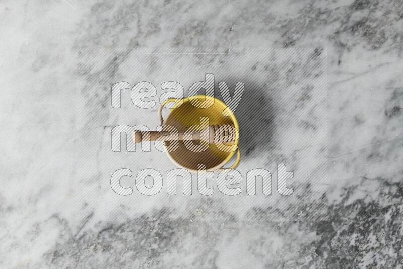 Multicolored pottery bowl with wooden honey dipper in it on grey marble background