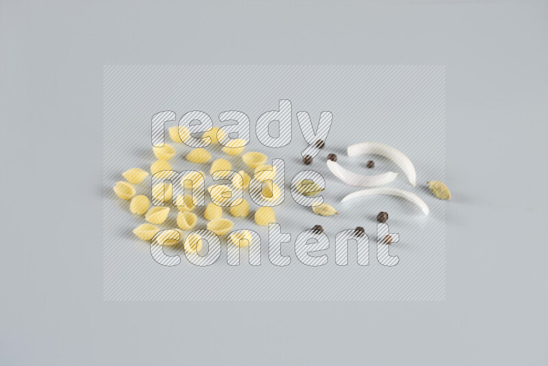 Raw pasta with different ingredients such as cherry tomatoes, garlic, onions, red chilis, black pepper, white pepper, bay laurel leaves, rosemary, cardamom and mushrooms on light blue background