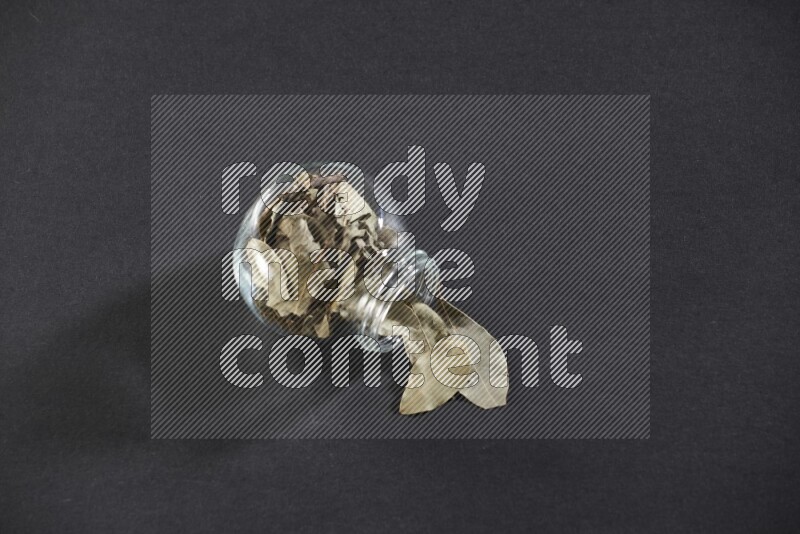 وعاء زجاجي ممتلئ بأوراق الغار والوعاء مقلوب وبعض الأوراق متناثرة خارجه علي خلفية سوداء