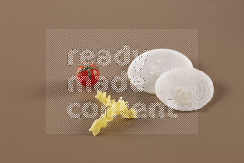 Raw pasta with different ingredients such as cherry tomatoes, garlic, onions, red chilis, black pepper, white pepper, bay laurel leaves, rosemary and cardamom on beige background