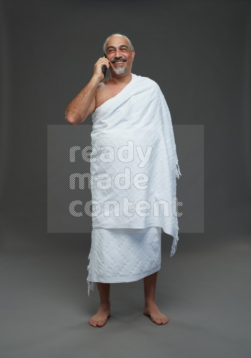 A man wearing Ehram Standing talking on phone on gray background