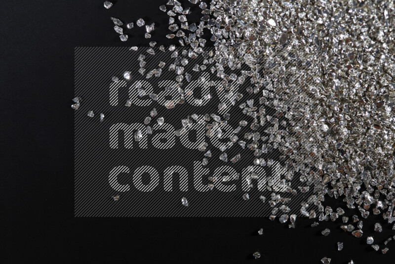 Silver shimmering fragments of glass scattered on a black background
