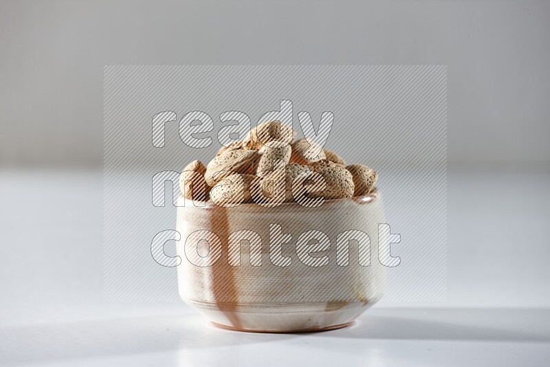A beige ceramic bowl full of almonds on a white background in different angles