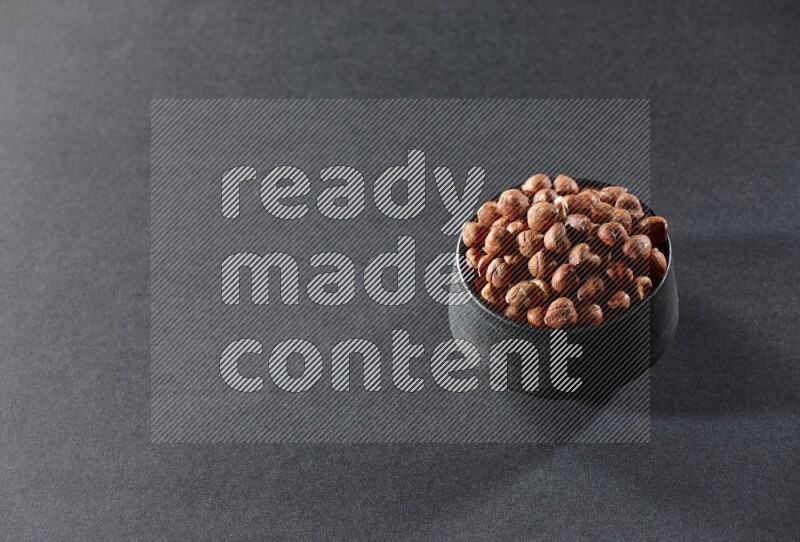 A black pottery bowl full of peeled hazelnuts on a black background in different angles