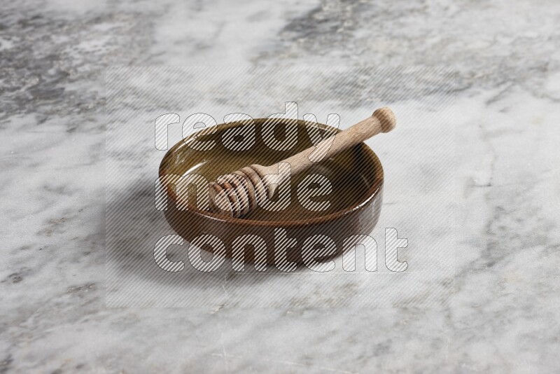 Multicolored Pottery Oven Plate with wooden honey handle in it, on grey marble flooring, 45 degree angel