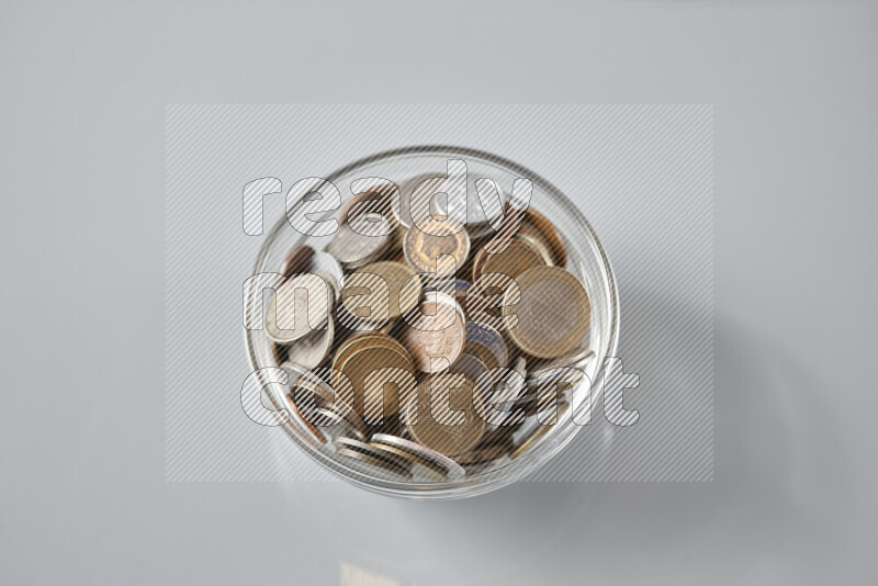 Random old coins in a glass bowl on grey background