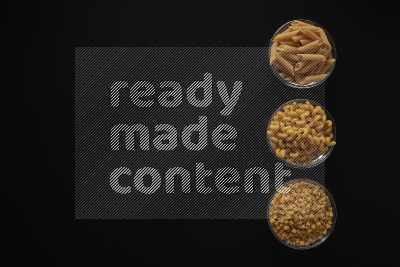 Different pasta types in 3 glass bowls on black background