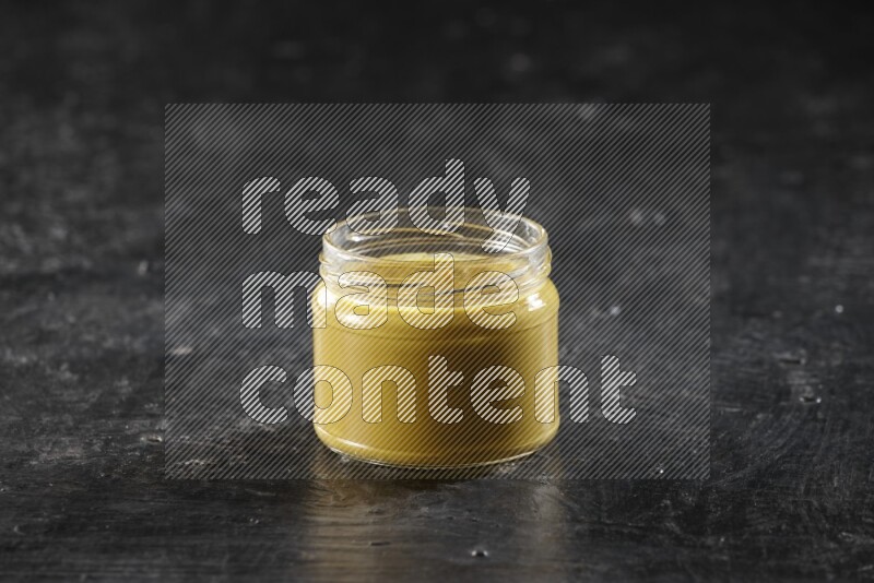 A glass jar full of mustard paste on a textured black flooring