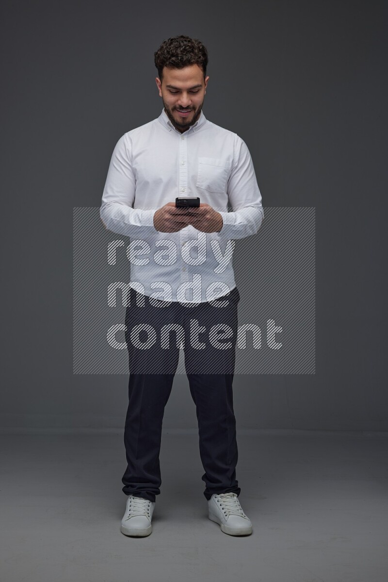 A man wearing smart casual standing and using his phone eye level on a gray background