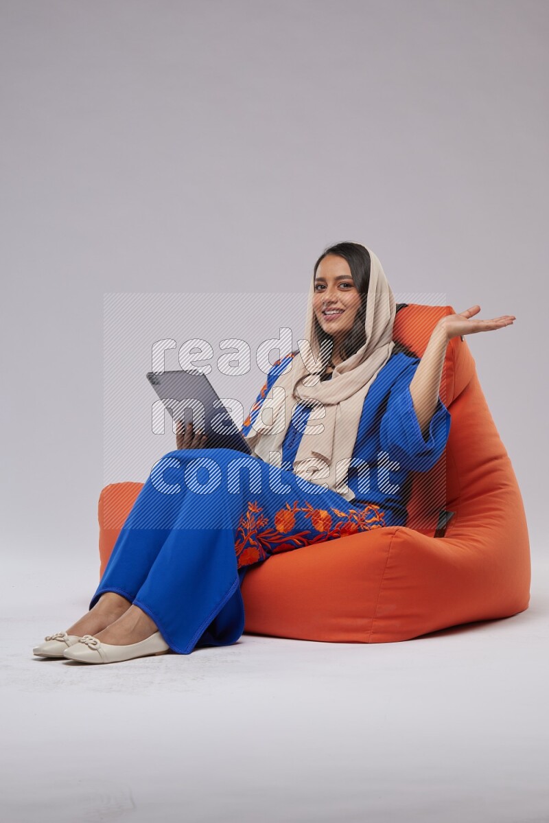 A Saudi woman sitting on an orange beanbag and working on tablet