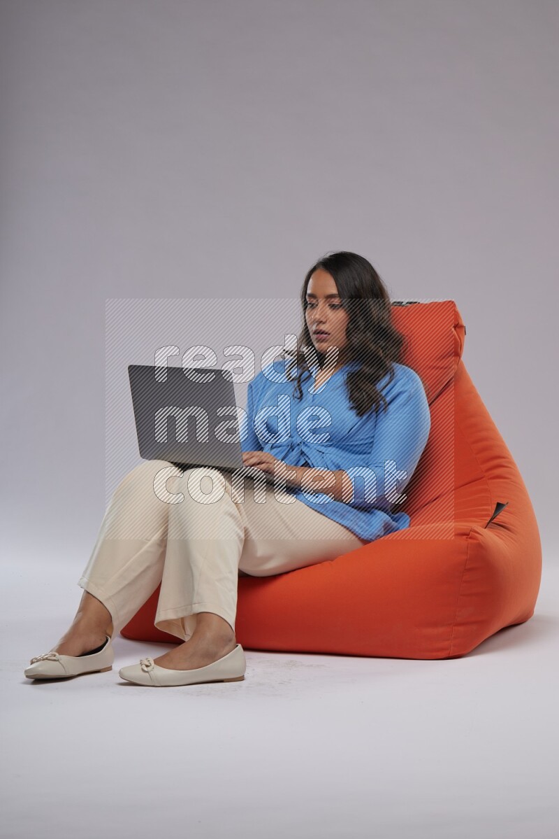 A woman sitting on an orange beanbag and working on laptop