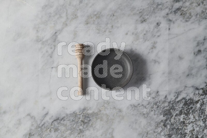 Black pottery bowl with wooden honey dipper on the side on grey marble background