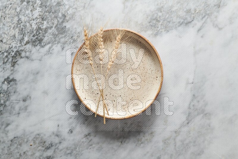 Wheat stalks on multicolored pottery plate on grey marble background