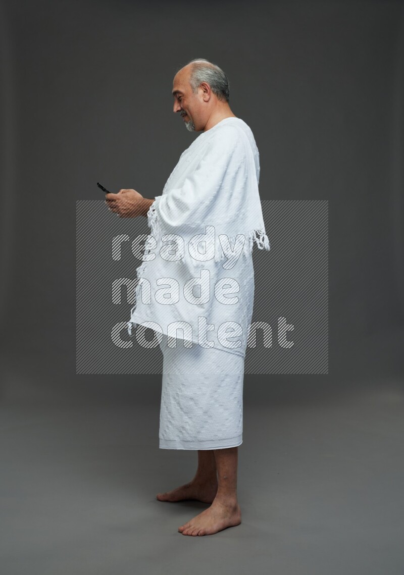 A man wearing Ehram Standing texting on phone on gray background