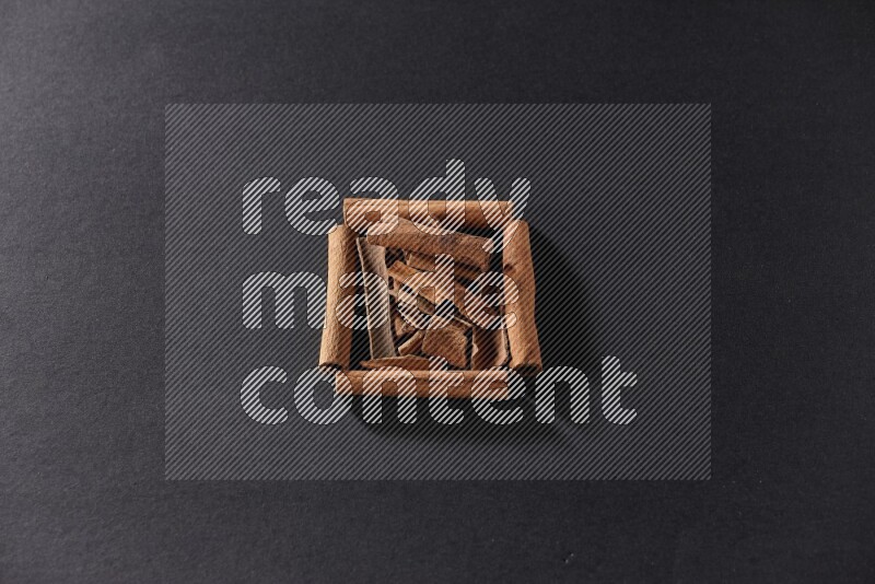 A single square of cinnamon sticks full of cinnamon on black flooring