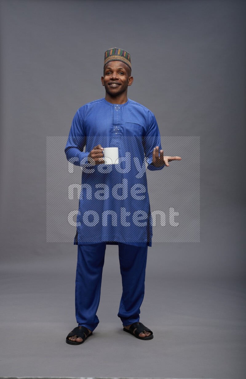 Man wearing Nigerian outfit standing holding mug on gray background