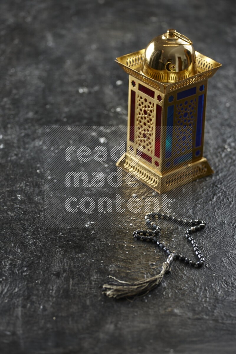 A golden lantern with different drinks, dates, nuts, prayer beads and quran on textured black background