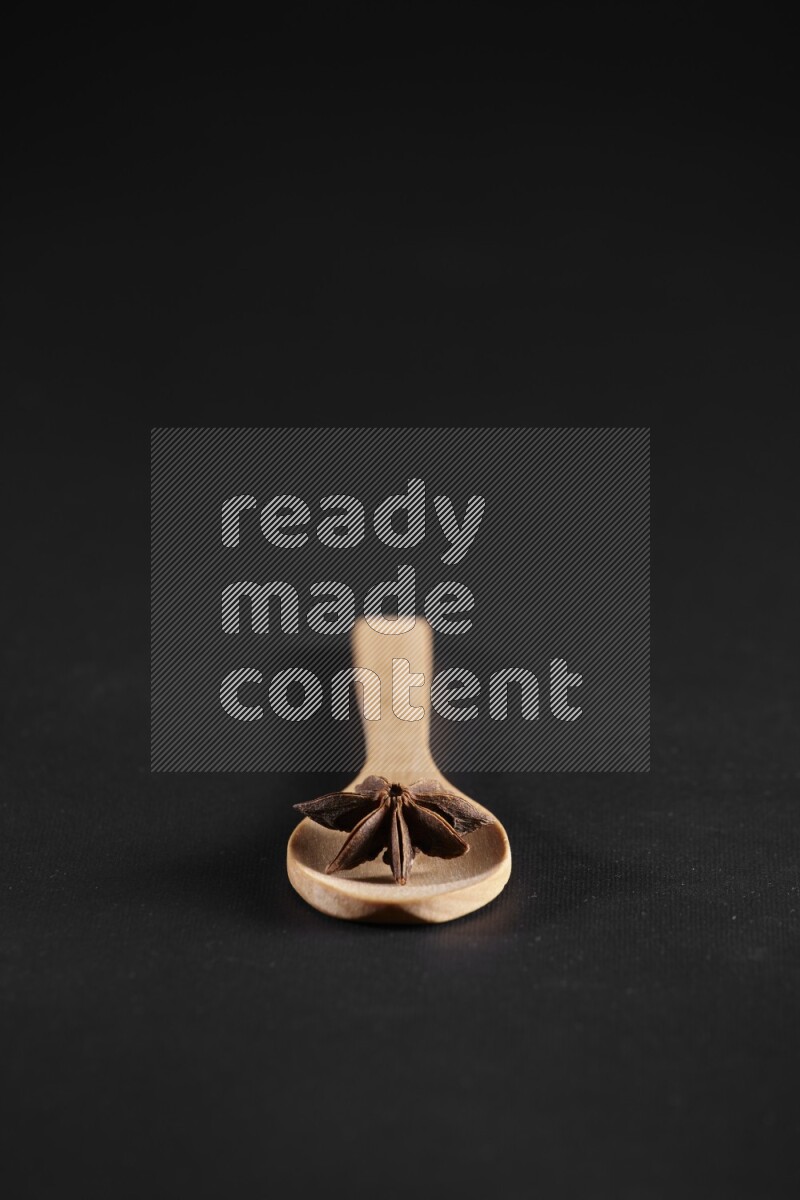 Star Anise in a wooden spoon on more stars anise filling the frame on black flooring