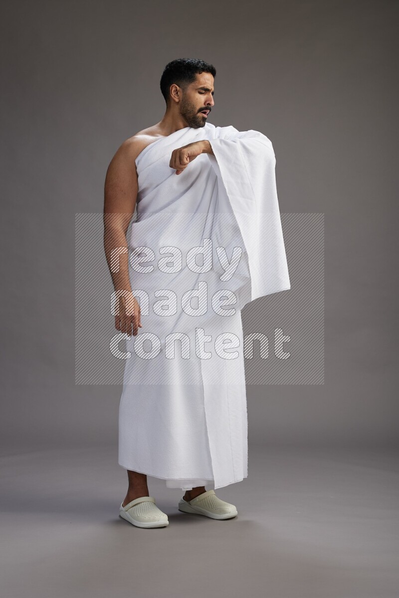 A man wearing Ehram standing showing how to sneeze on gray background