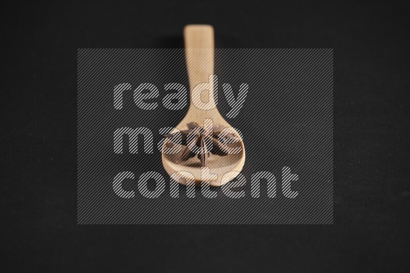 Star Anise in a wooden spoon on more stars anise filling the frame on black flooring