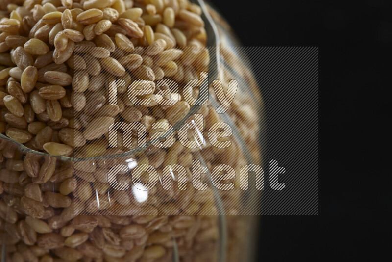 Hulled wheat in a glass jar on black background