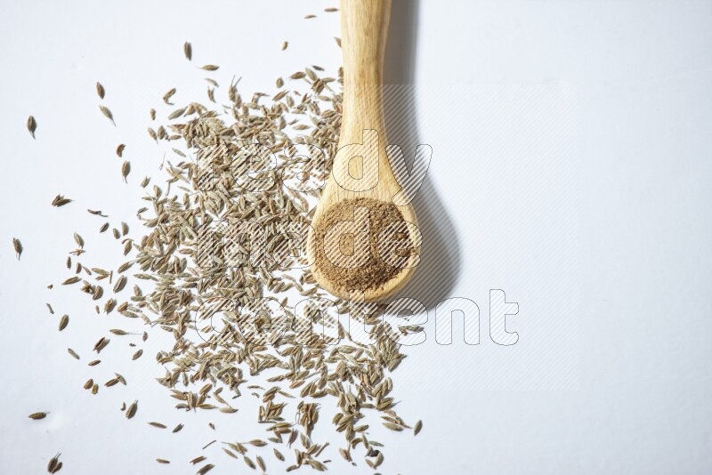 A wooden spoon full of cumin powder and cumin seeds beside it on white flooring
