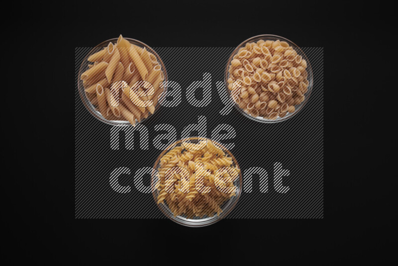 Different pasta types in glass bowls on black background