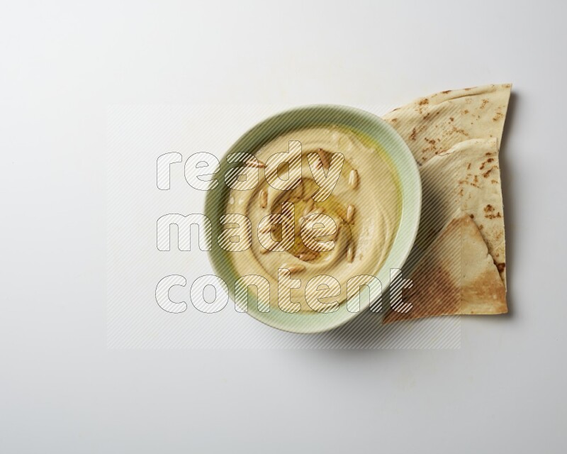 Hummus in a green plate garnished with pine nuts on a white background
