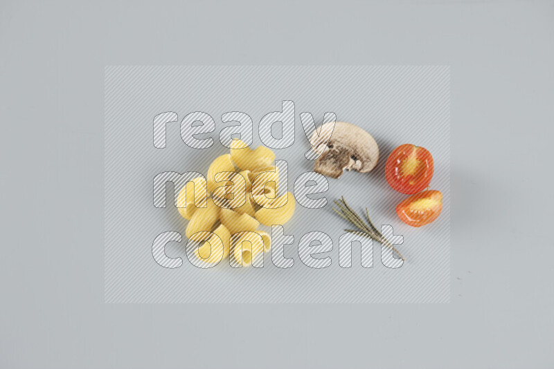 Raw pasta with different ingredients such as cherry tomatoes, garlic, onions, red chilis, black pepper, white pepper, bay laurel leaves, rosemary, cardamom and mushrooms on light blue background