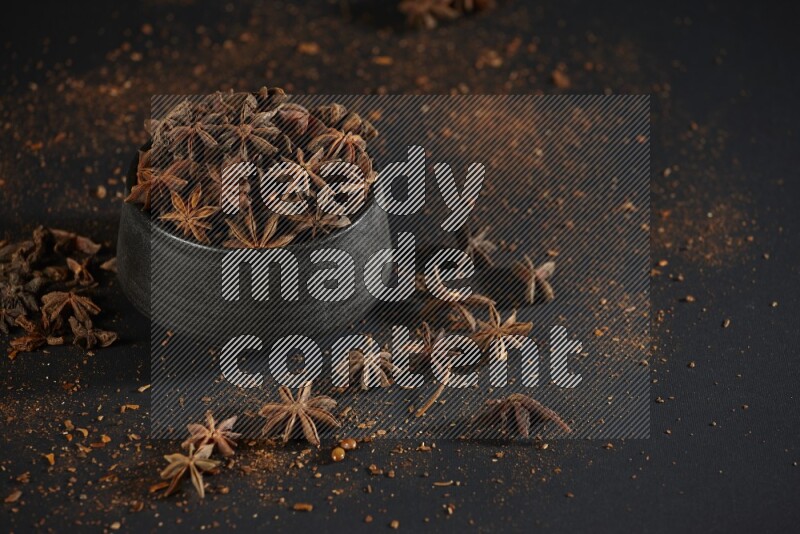 Star Anise in a black bowl with sprinkled anise on black flooring