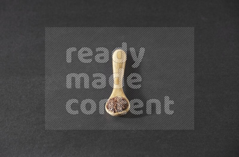 A wooden spoon full of flaxseeds on a black flooring