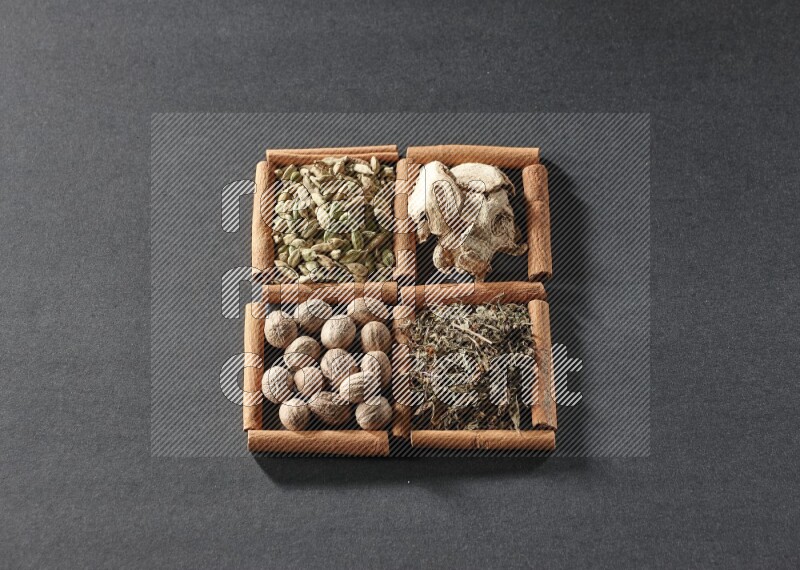 4 مربعات من عيدان القرفة ممتلئة بالريحان المجفف والهيل والزنجبيل المجفف وجوزة الطيب على أرضية سوداء