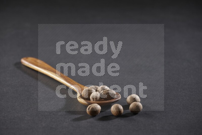 A wooden ladle full of whole nutmeg seeds on a black flooring