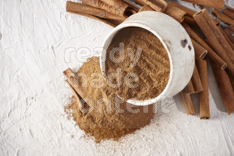 Ceramic beige bowl over filled with cinnamon powder and cinnamon sticks around the bowl on a textured white background in different angles