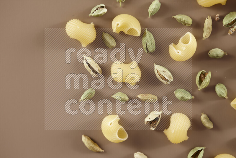 Raw pasta with different ingredients such as cherry tomatoes, garlic, onions, red chilis, black pepper, white pepper, bay laurel leaves, rosemary and cardamom on beige background