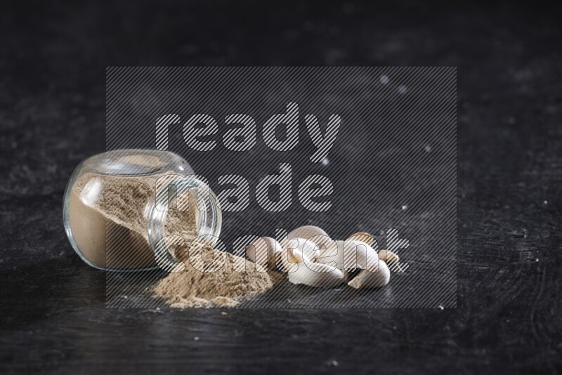 A glass spice jar full of garlic powder flipped over with the powder came out on a textured black flooring